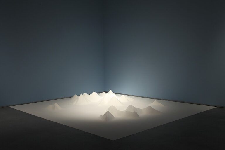 A white sheet on a gallery floor with mountain forms within it