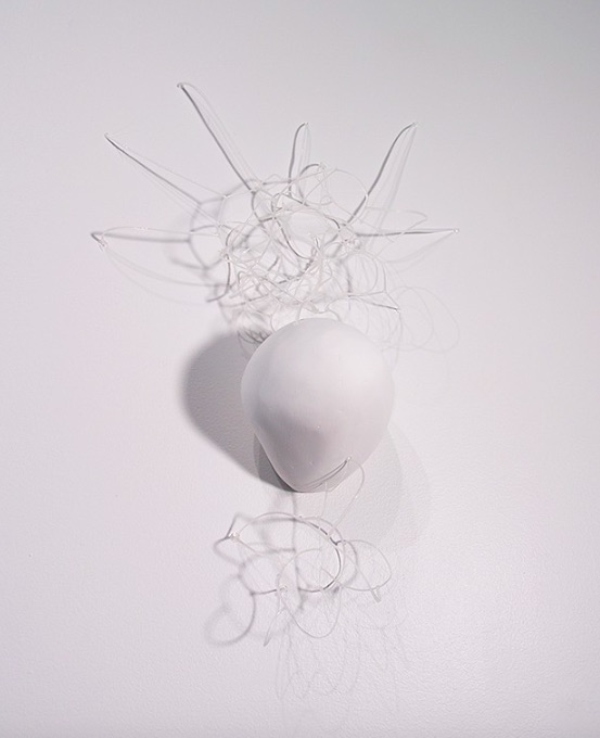 An irregular round white sculpture on a white background with netting