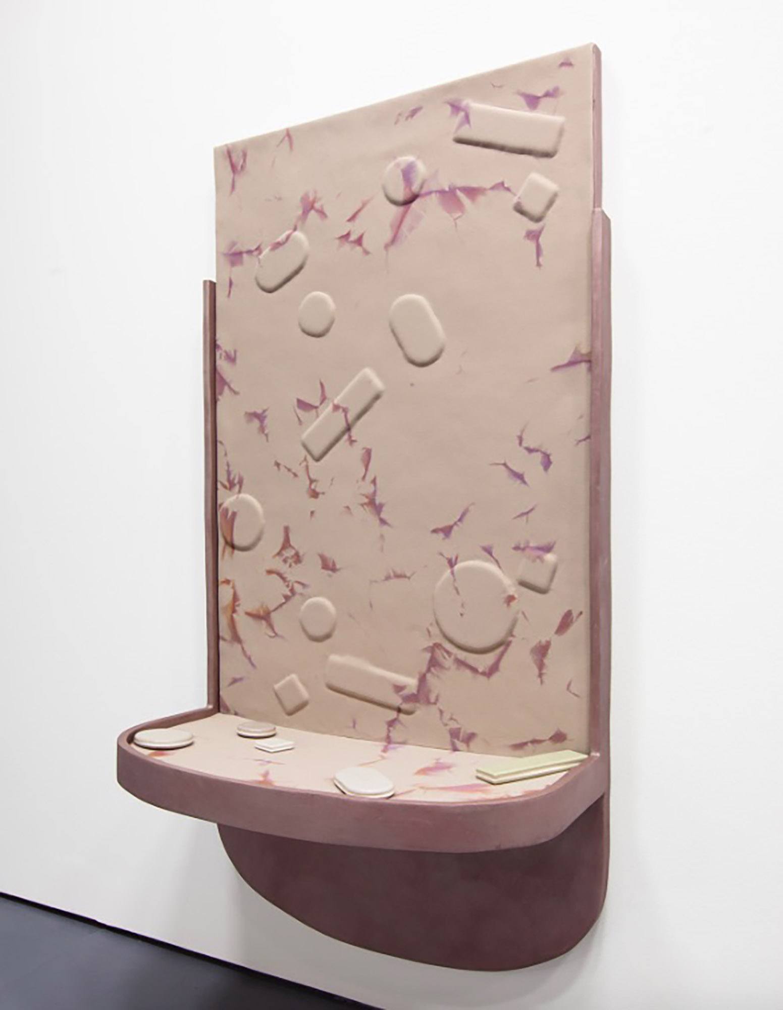 A mauve and light pink slab of clay molded into a shelf with molded shapes on its surface