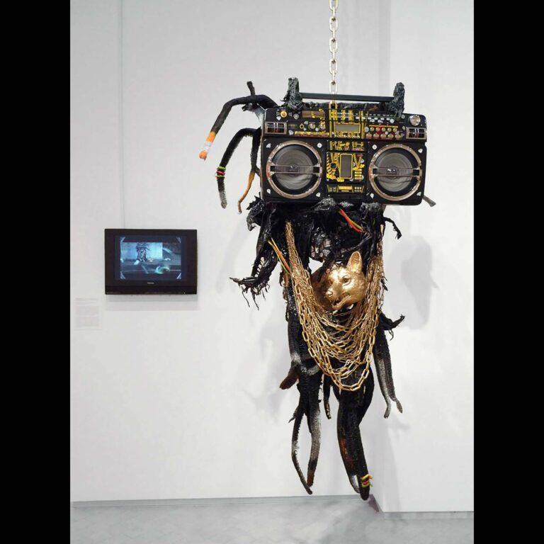A hanging sculpture of a boom box, gold chains, a gold animal head, and other components