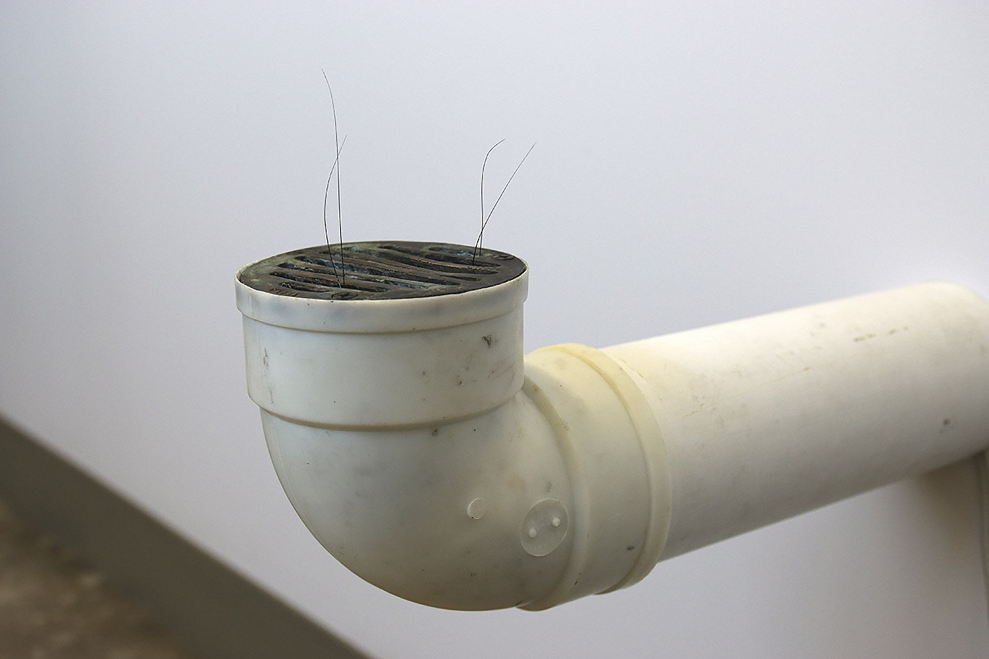 A pipe coming out of a wall with a drain and four hairs sticking from it