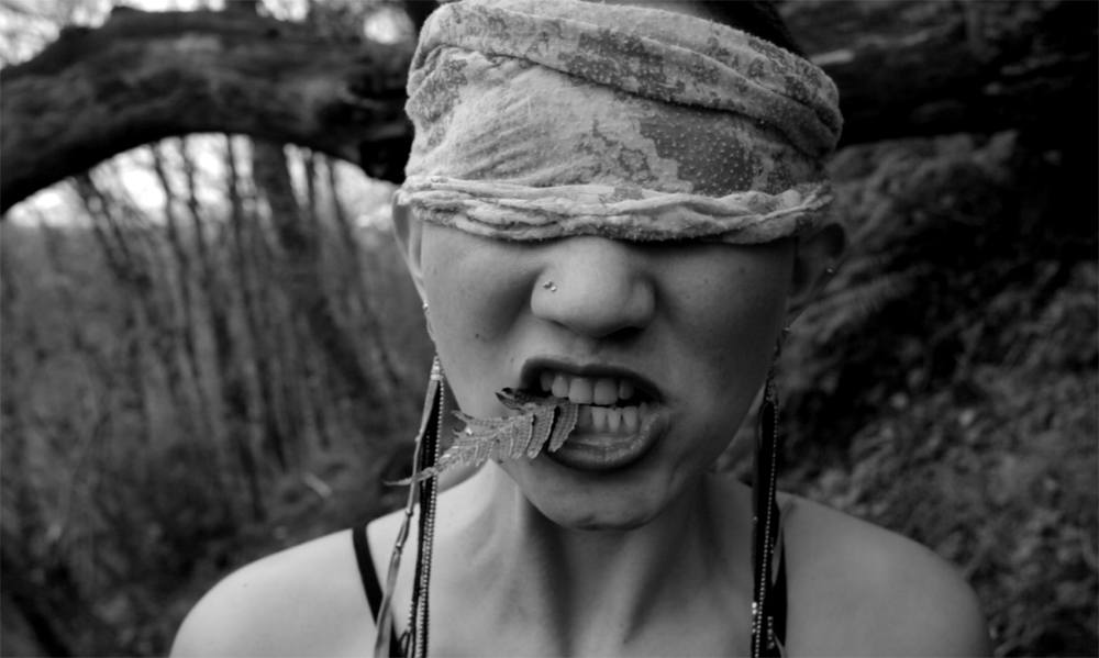 a black and white image of a blindfolded woman with a leaf held between her teeth