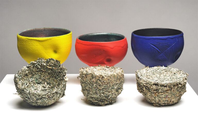 Three colored pots in yellow, red, and blue, behind three sculptures of shredded material that appear they were molded inside the pots