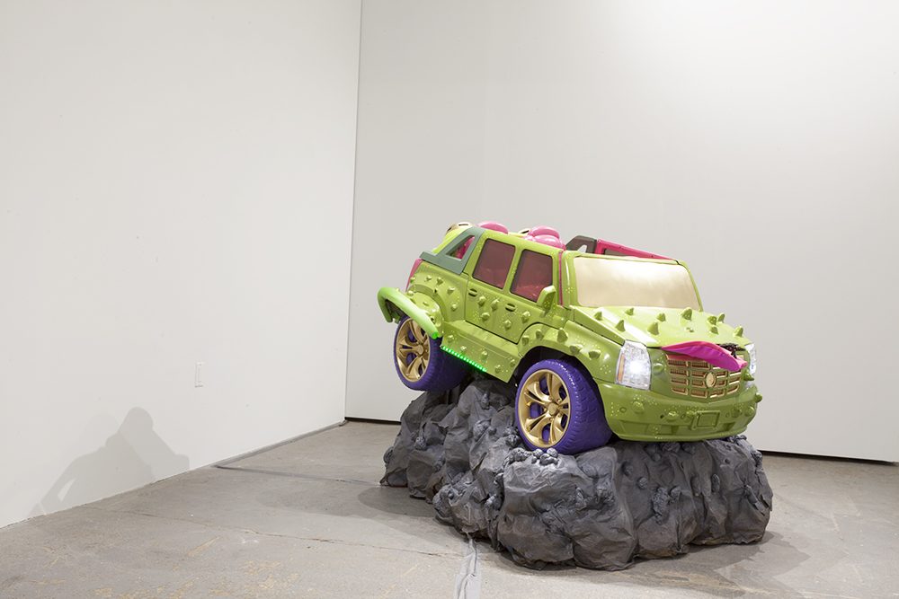 An installation image of a sculpture of a car on a rock