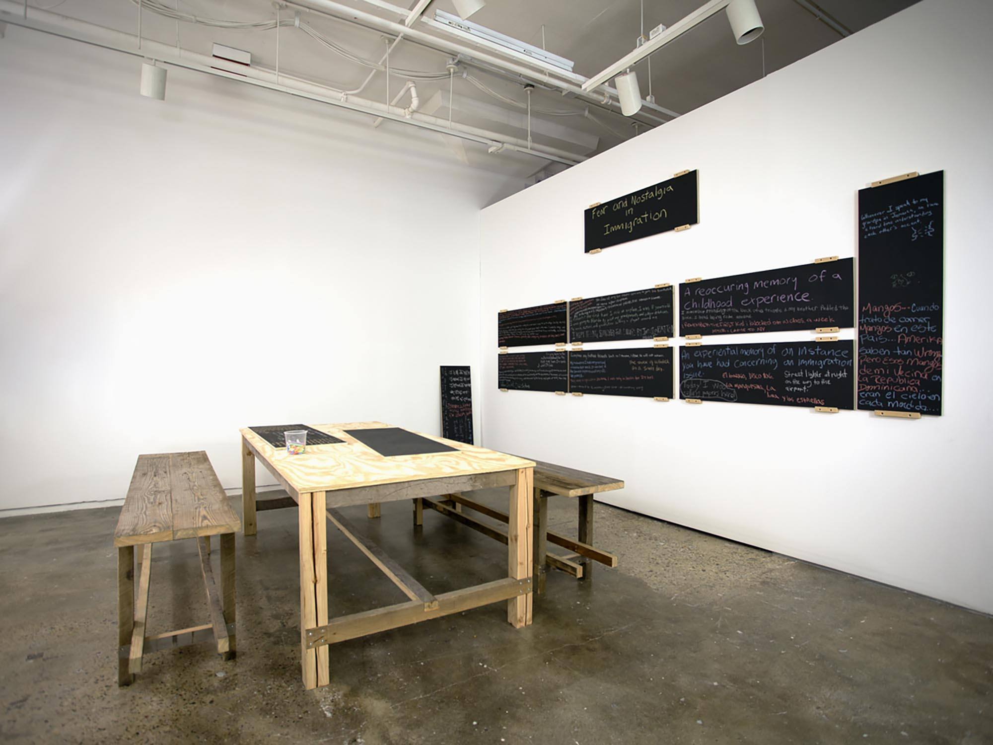 A gallery space with a wooden table and benches and chalkboards on the wall