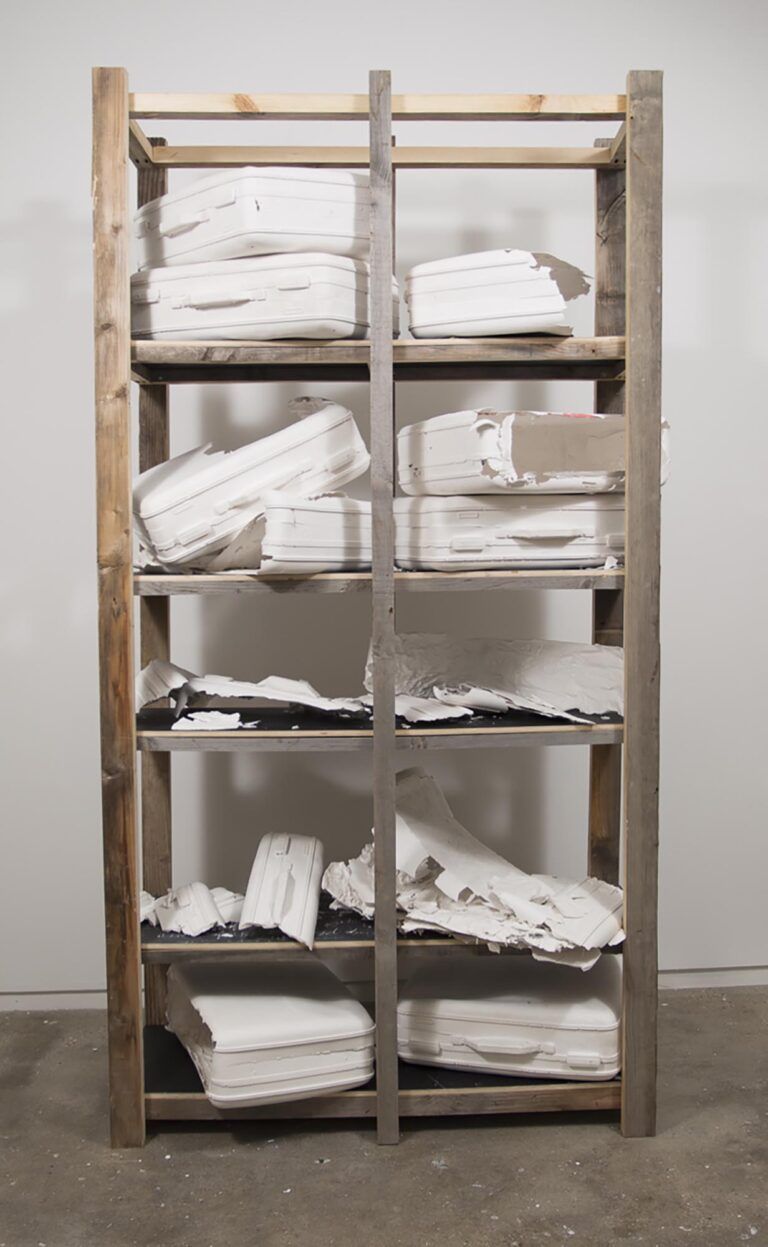 A wooden rack in a gallery space with white casts of suitcases