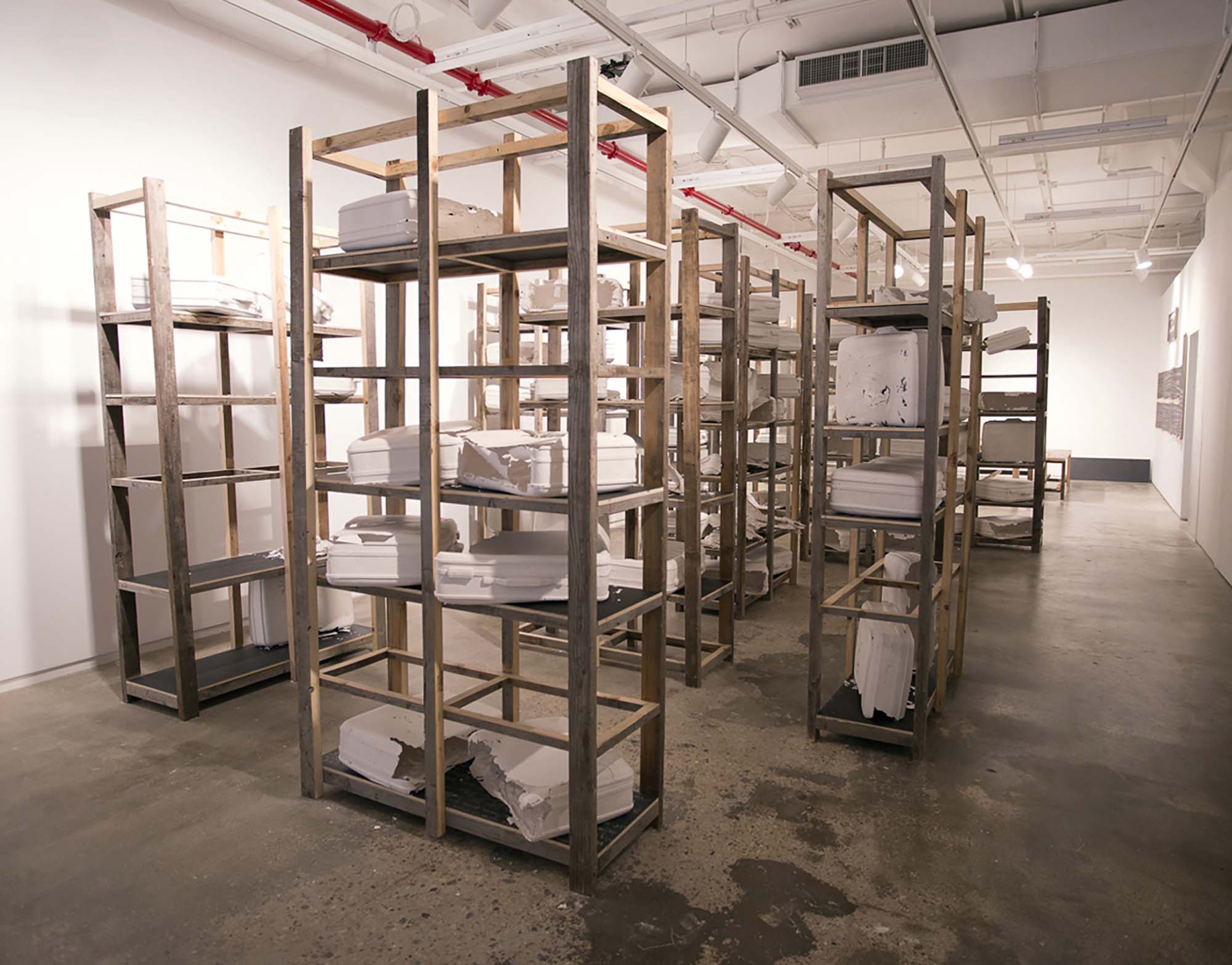 Wooden racks in a gallery space with white casts of suitcases