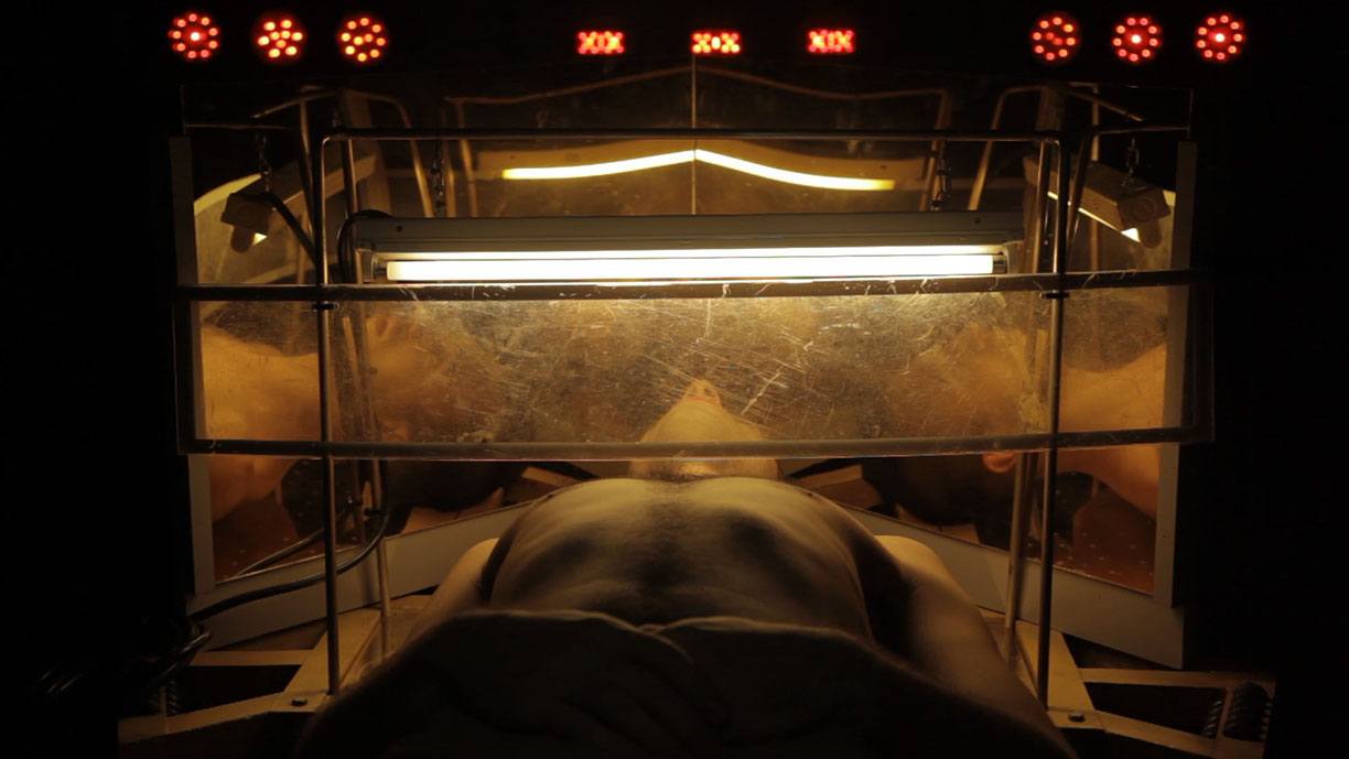 A person laying with their torso and head inside a constructed object containing lights and mirrored surfaces