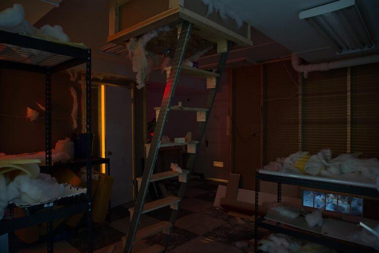 An unfinished room with construction materials and a ladder coming from the ceiling