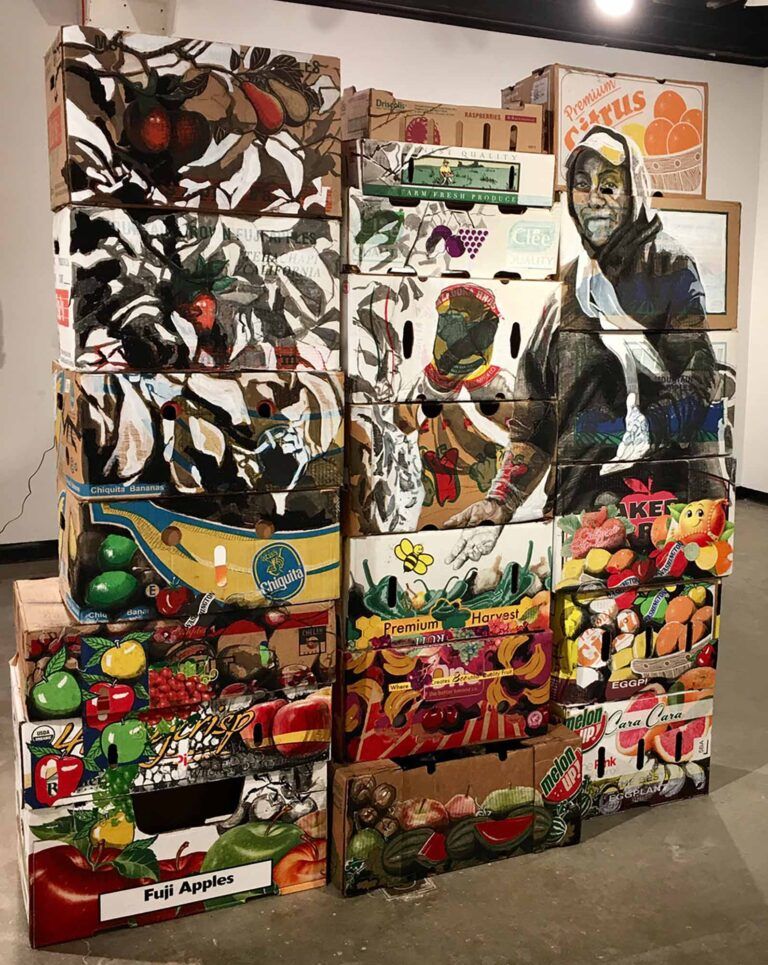 Painted produce boxes with portraits of farmworkers arranged in a tower