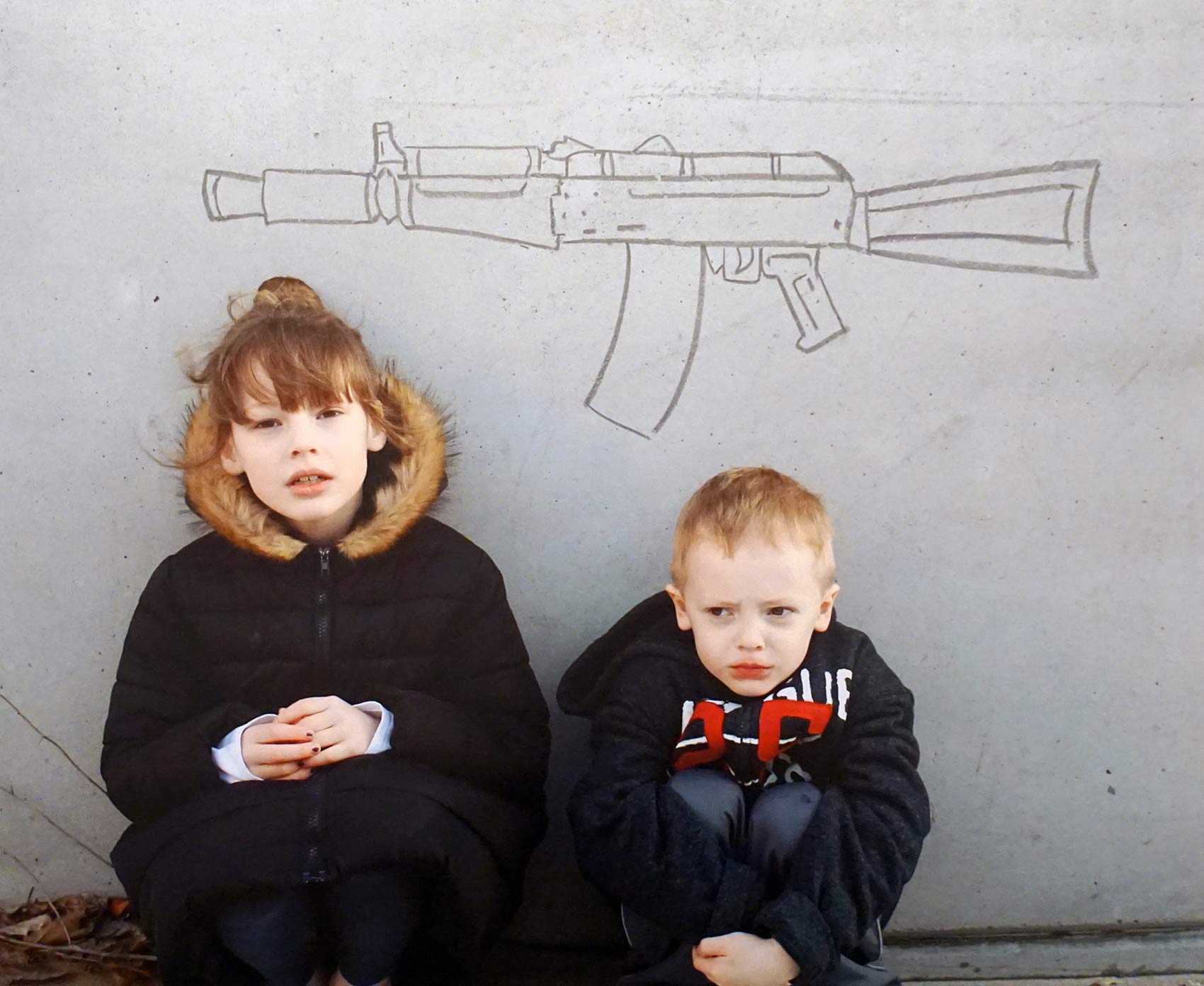 A photograph of two children with a gun drawn on the wall behind them
