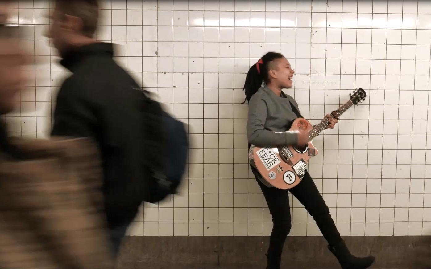 A person singing and playing guitar in a subway station
