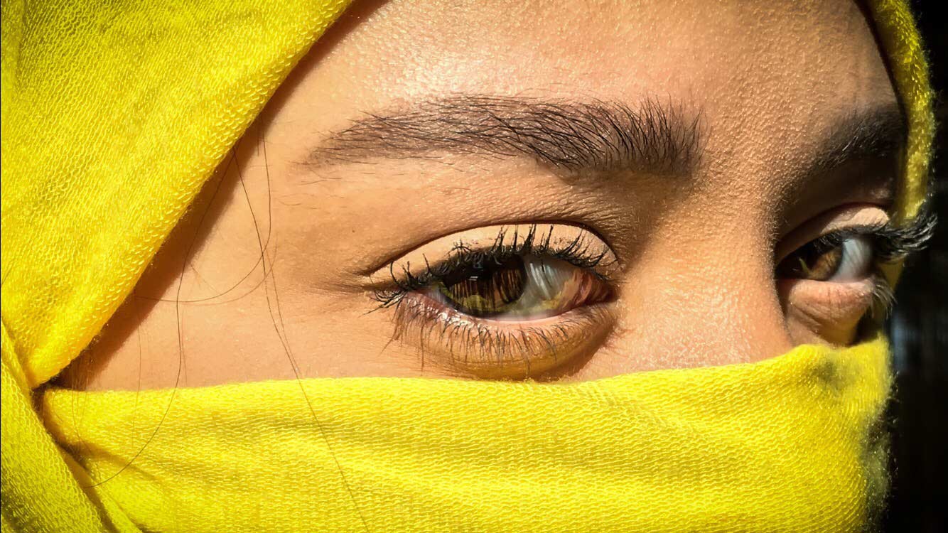 a photograph of a woman's face, partially covered by a yellow head covering