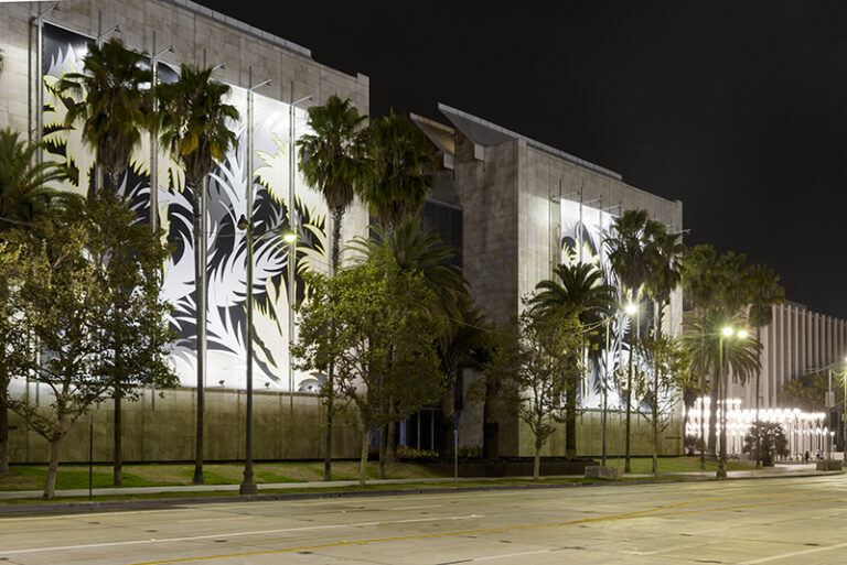 A photograph of large concrete buildings, each with a mural of abstract leaves