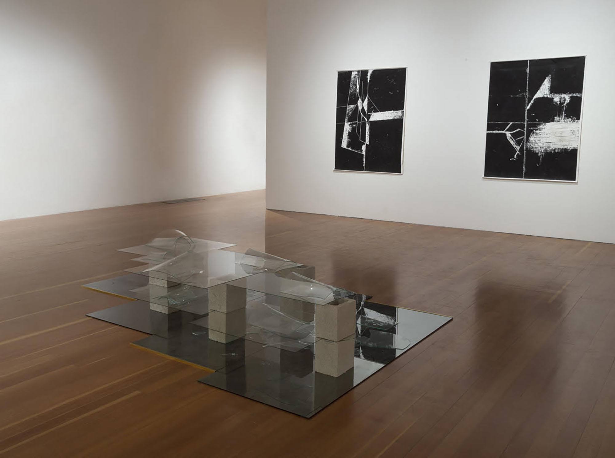 An installation view of a glass and concrete sculpture with two framed black and white images in the background