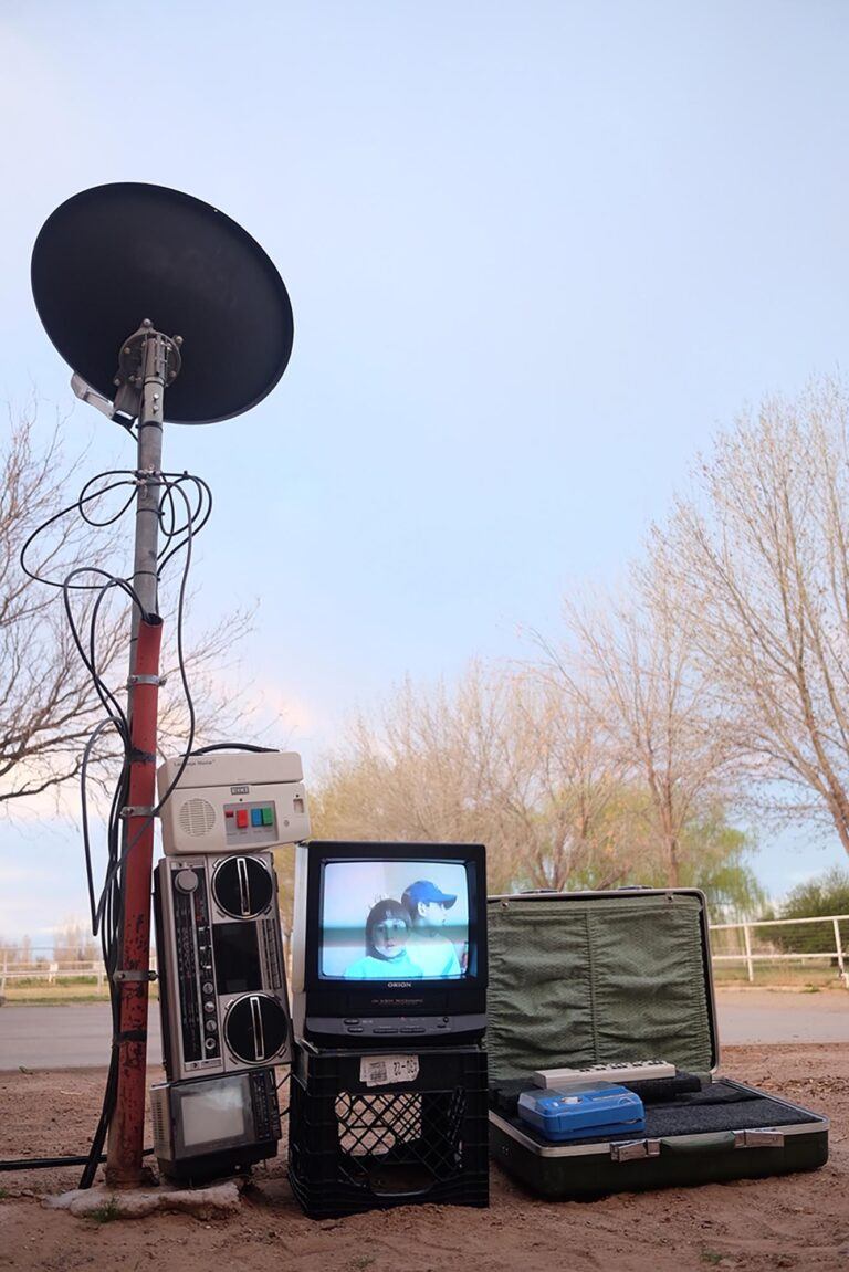 A satellite, television, and other equipment in a stack outside in the sand