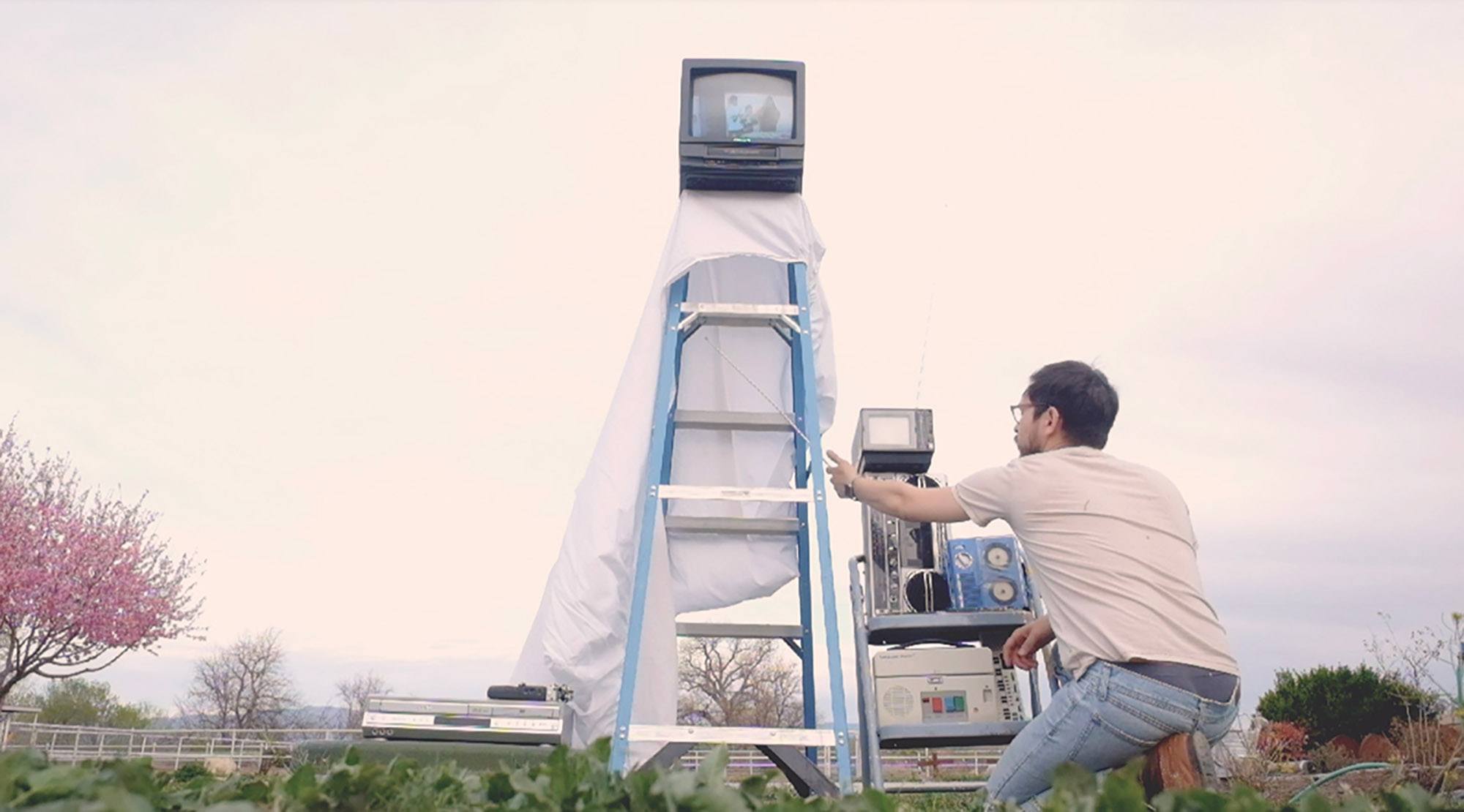 A man controls a small television on top of a ladder