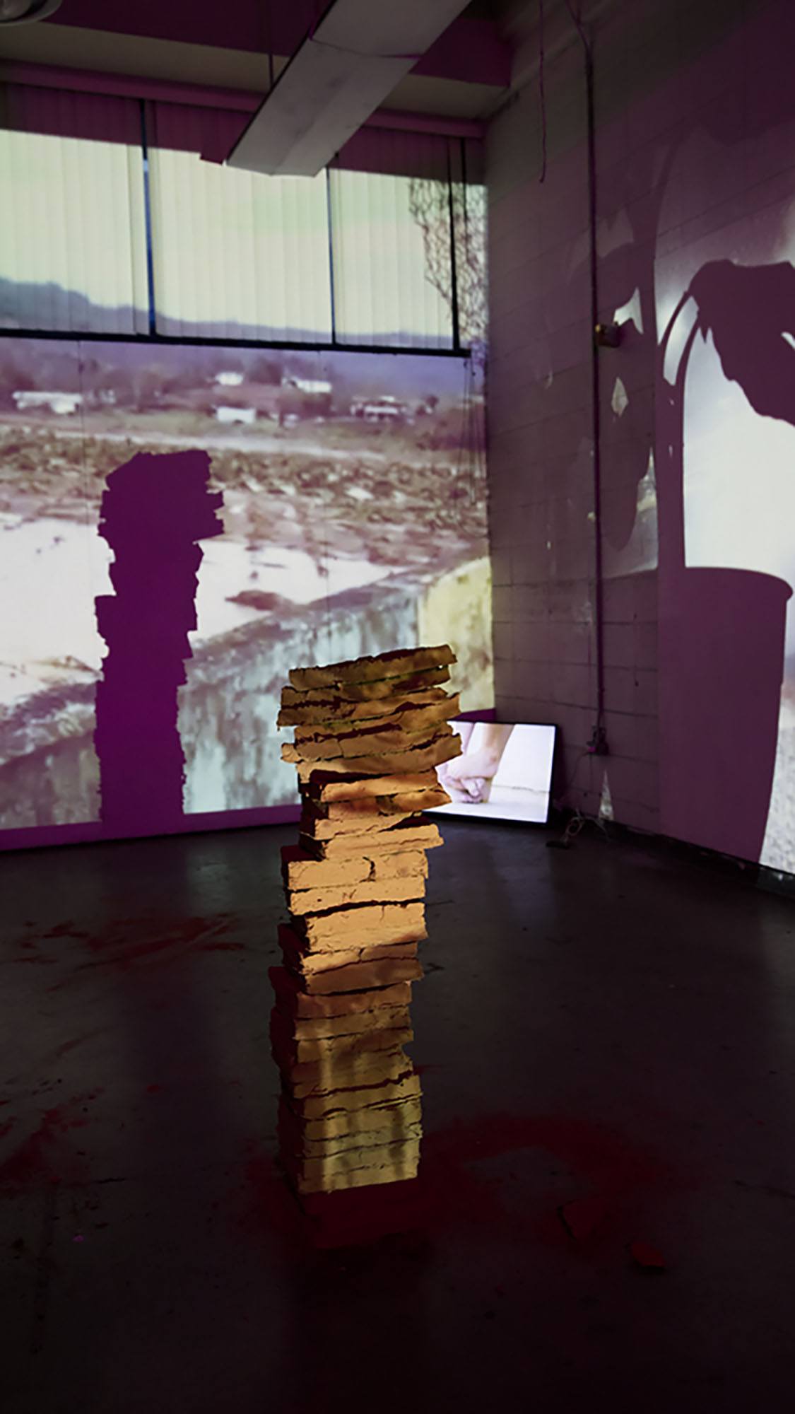 A stack of adobe tiles on a gallery floor with projections on the walls