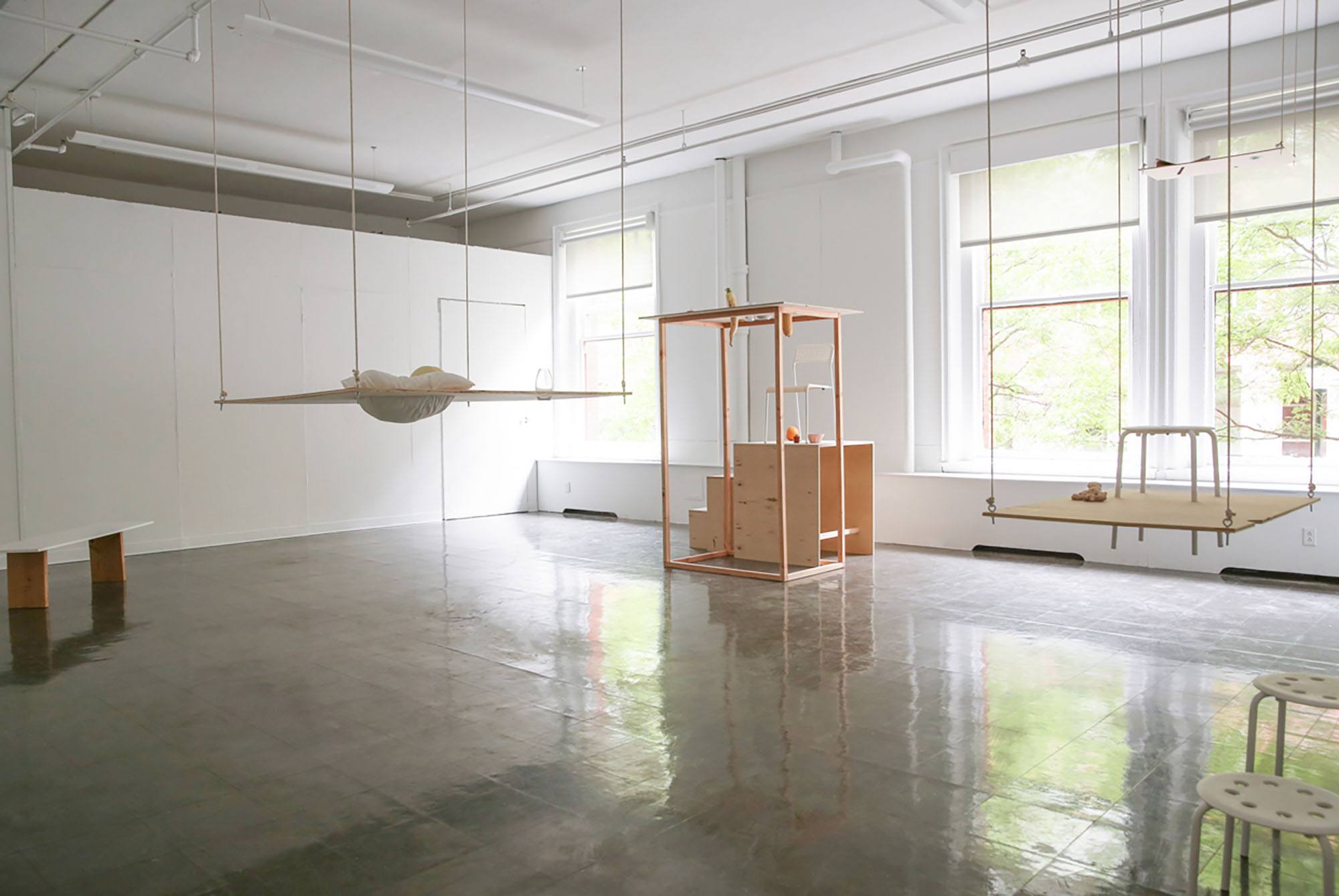 An installation view of suspended and constructed wood surfaces with objects cutting through them