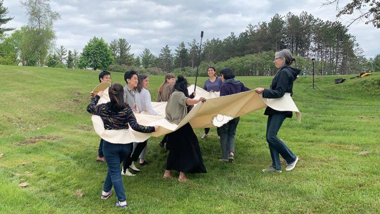 Ten people connected at the waist by a canvas tarp