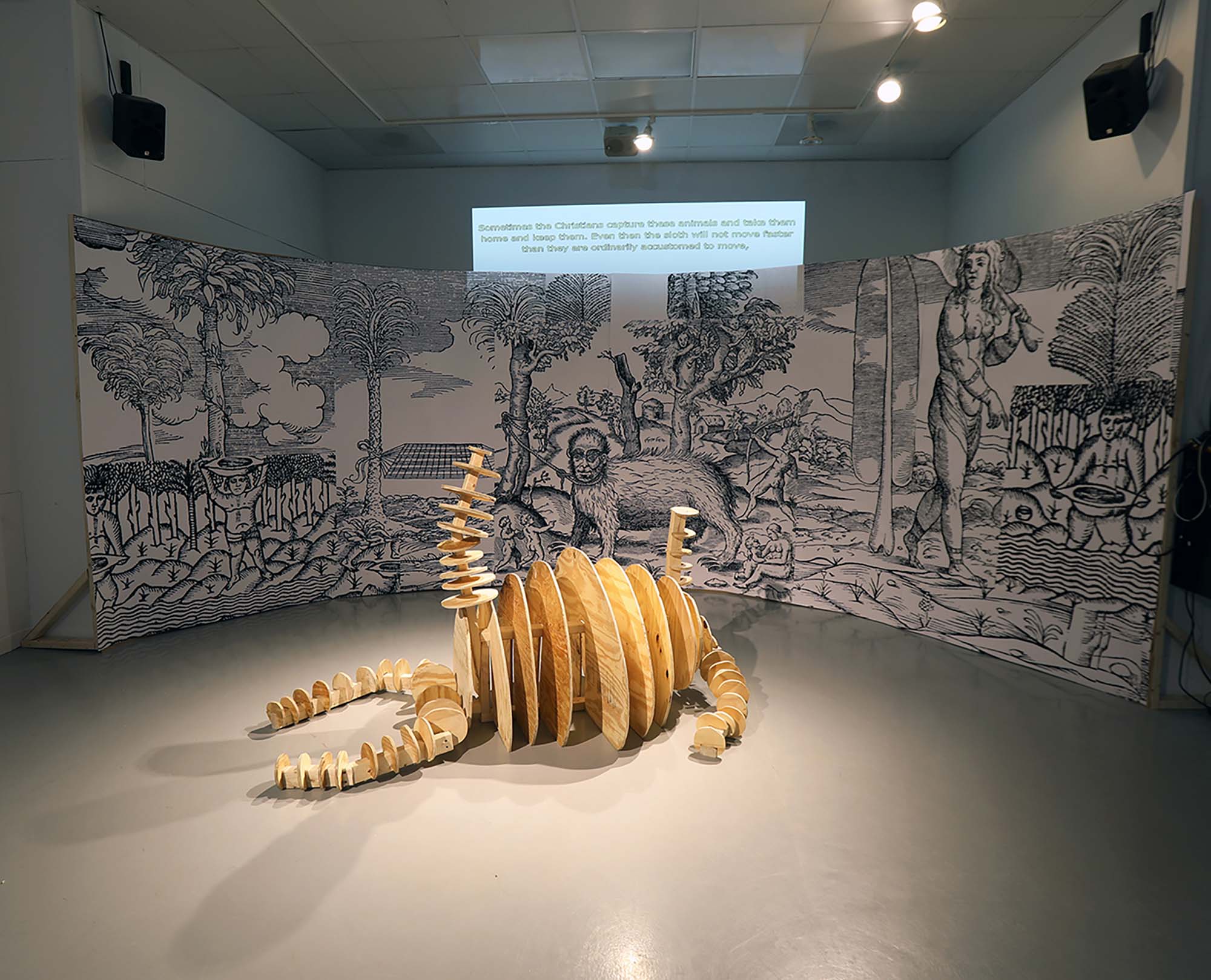 A wooden sculpture made from rows of cut partial circles on a gallery floor with a large illustration behind