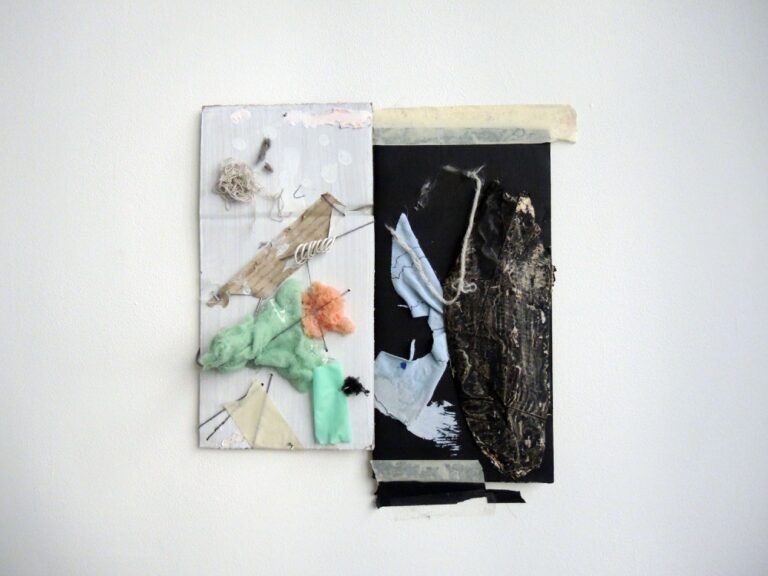 An installation image of a collaged artwork that is white on one side and black on the other, containing foam and fabric pieces