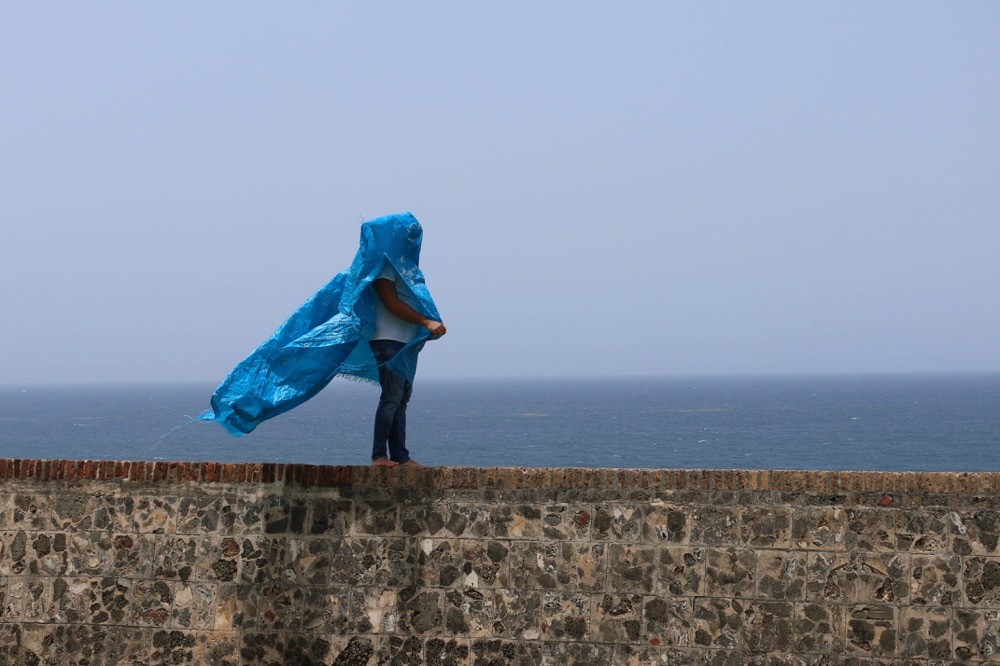 An image of a person standing on a retaining wall near the ocean, with blue plastic shading their head