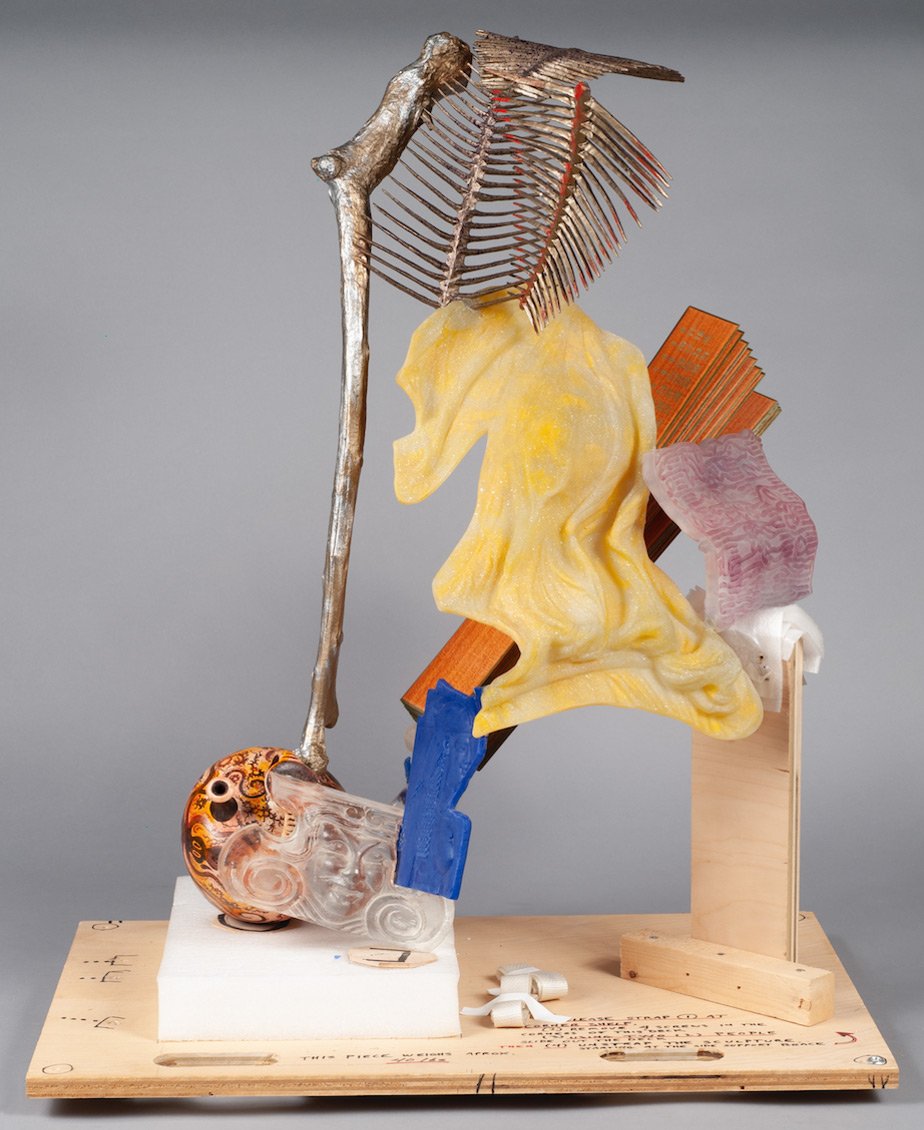 An abstract sculpture in yellow, orange, blue and bronze on a wooden base