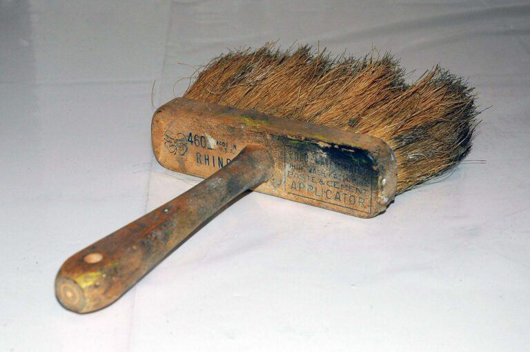 A used paste and cement applicator brush with paint and worn out text on the handle