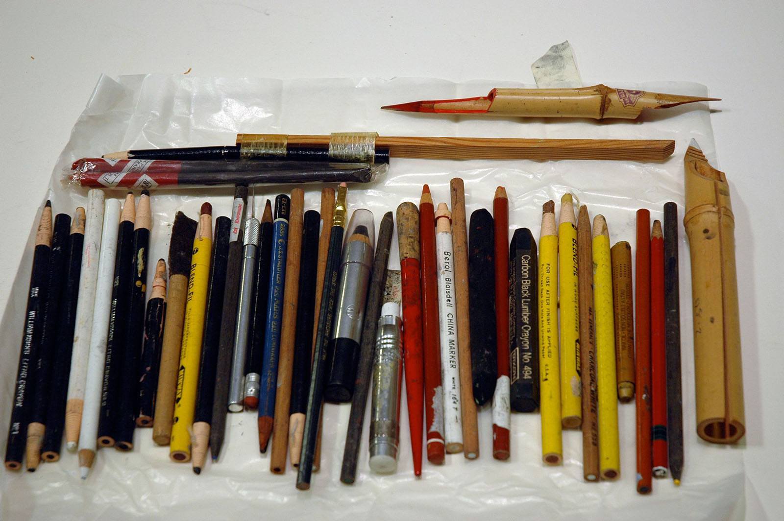 Assorted used drawing tools including conte crayons, charcoal, colored pencils, and bamboo utensils