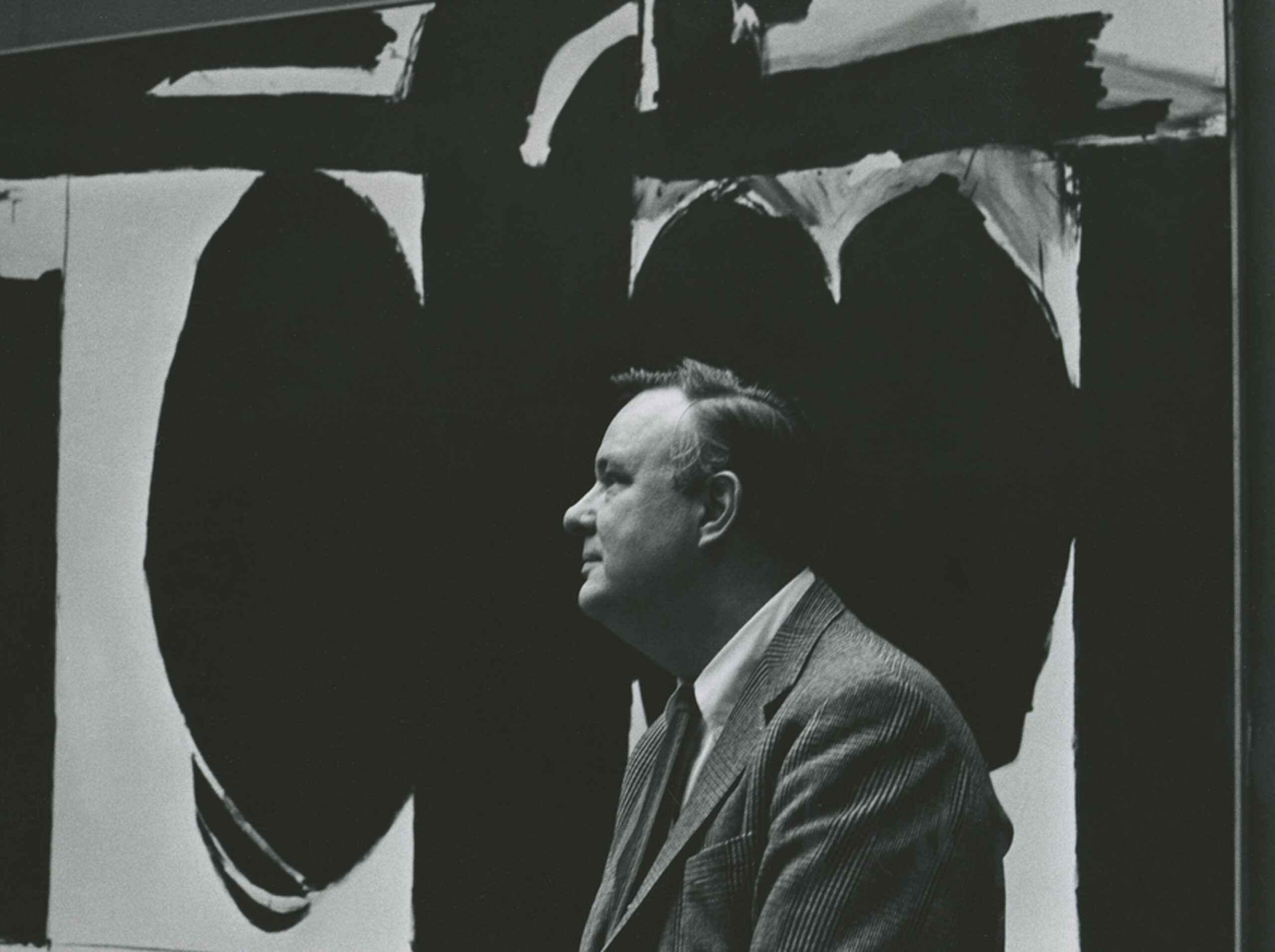 A side portrait of Robert Motherwell posing in front of an Elegy painting